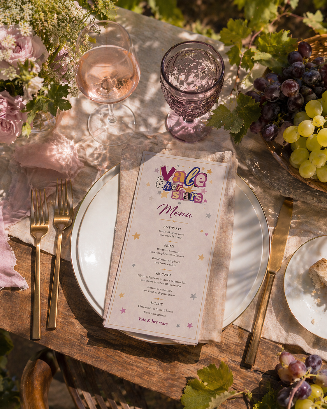 Menu Vale & her stars su tavola apparecchiata con calici, uva e fiori - dettagli curati di un'esperienza su misura